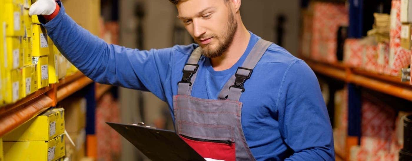 A person is shown with a clipboard taking parts off of a shelf.