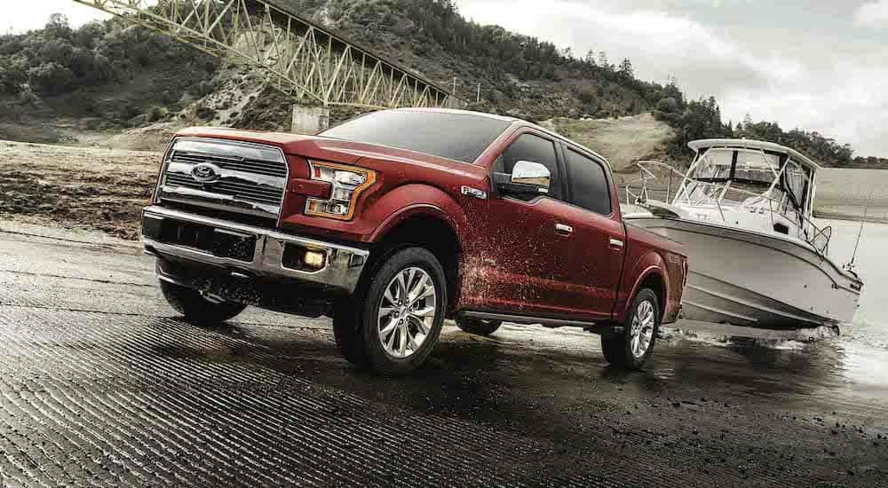 A red 2017 Ford F-150 is shown from the front at an angle while towing a boat after leaving a dealer that has used trucks for sale.