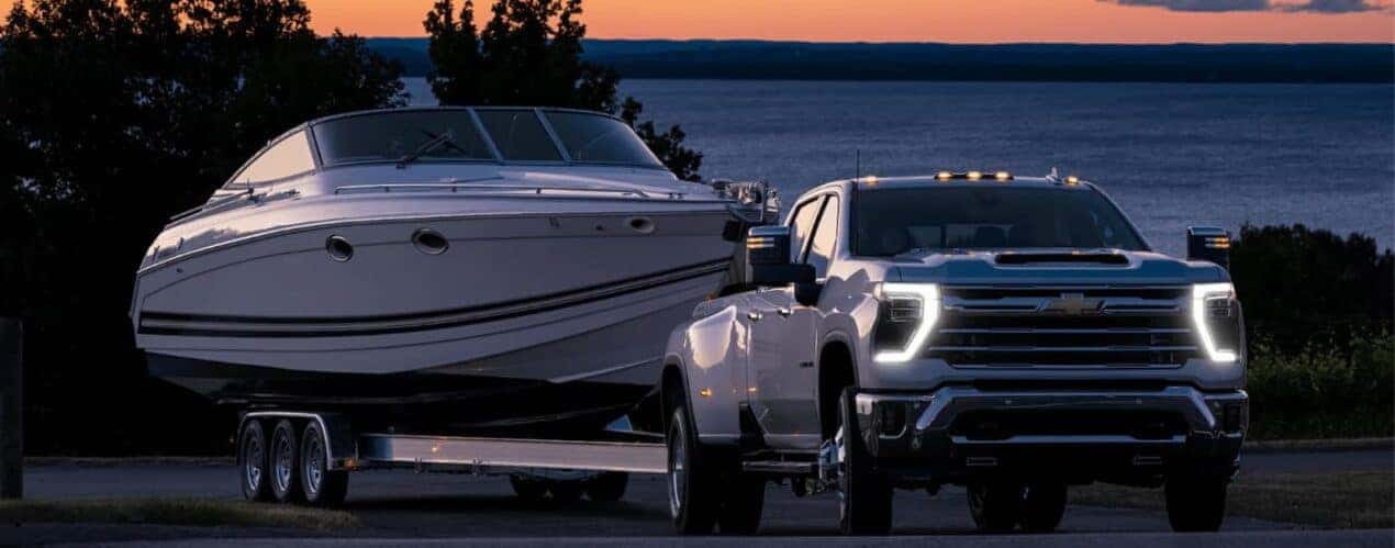A white 2024 Chevy Silverado 3500 HD is shown towing a white fishing boat.