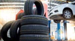A stack of summer tires are shown near a white sedan on a lift.