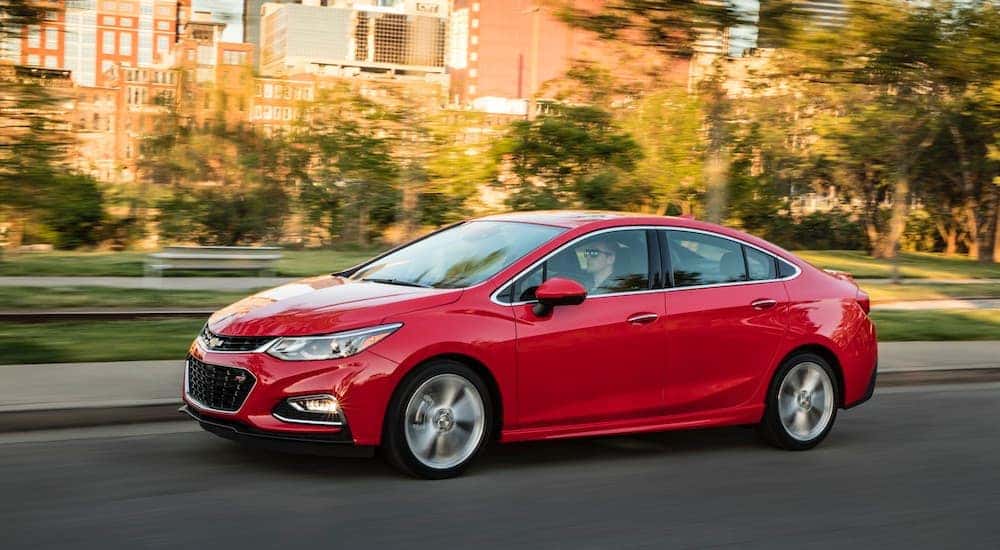 A red 2016 Chevy Cruz is shown from the side after leaving a dealer that has used cars for sale.