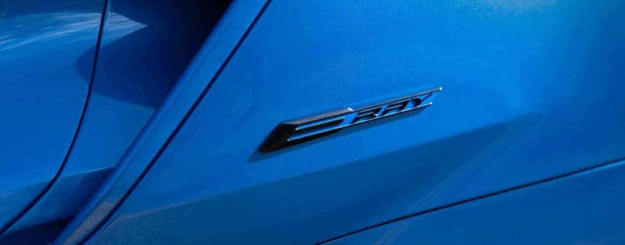 A close up shows the 'E-Ray' badge on a blue 2024 Chevy Corvette E-Ray 3LZ.