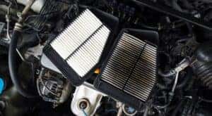 A clean and dirty air filter are shown resting on a vehicle engine.