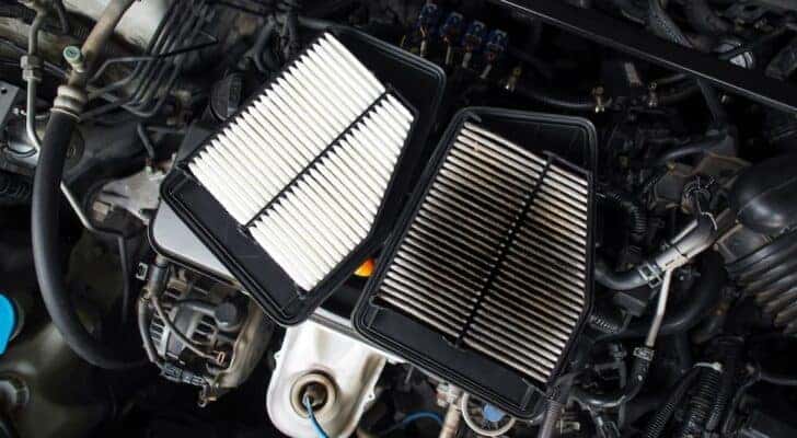 A clean and dirty air filter are shown resting on a vehicle engine.