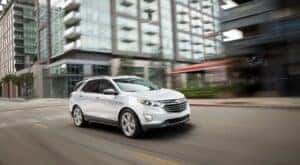 A white 2018 Chevy Equinox is shown driving on a city street after viewing cheap used cars for sale.
