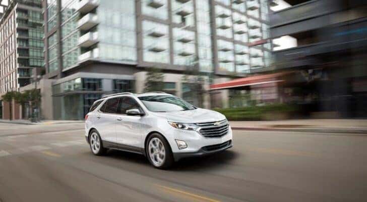 A white 2018 Chevy Equinox is shown driving on a city street after viewing cheap used cars for sale.