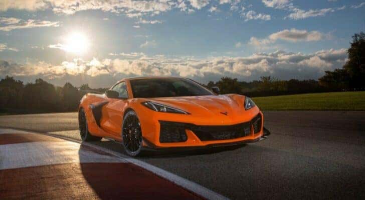 An orange 2023 Chevy Corvette Z06 is shown on a racetrack on a sunny day.