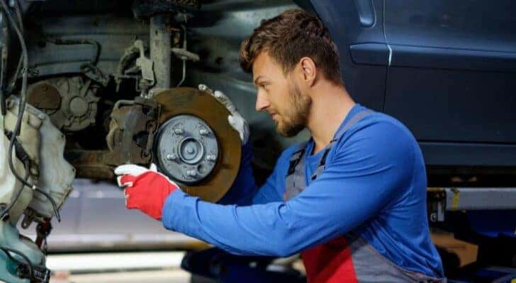 A mechanic is shown inspecting a rusty brake rotor.