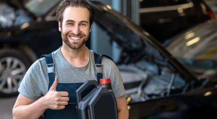 A mechanic is shown giving a thumbs up and holding a container of oil.