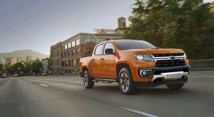 An orange 2021 Chevy Colorado Z71 is shown driving on a city road after viewing used trucks for sale near Dayton.