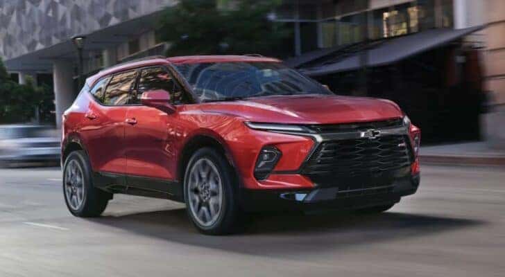 A red 2023 Chevy Blazer is shown driving to a Chevy dealer near Loveland.