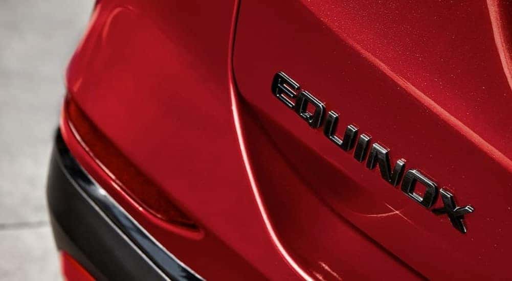 A close-up of a Equinox badge on the tailgate of a red 2024 Chevy Equinox is shown.