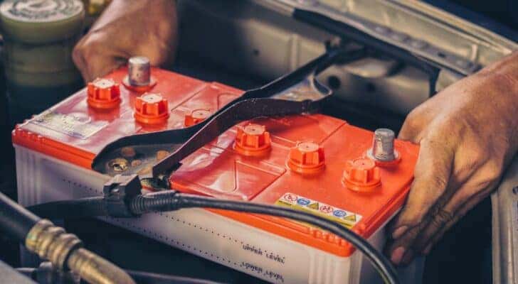 A close-up on a car battery being placed into an engine is shown.