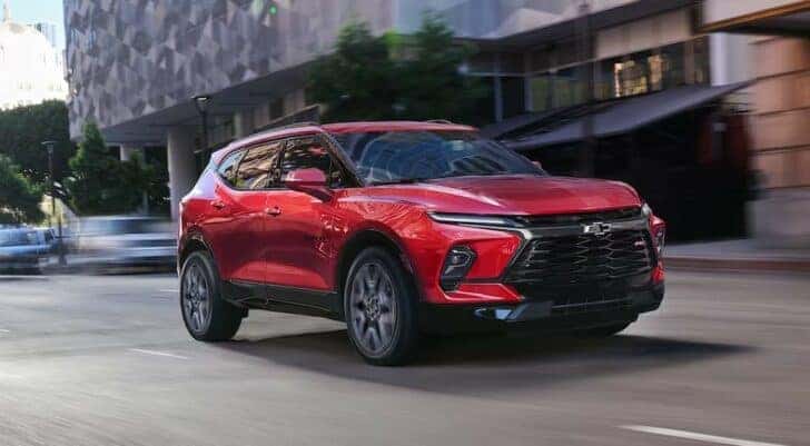 A red 2024 Chevy Blazer RS is shown driving on a city street.