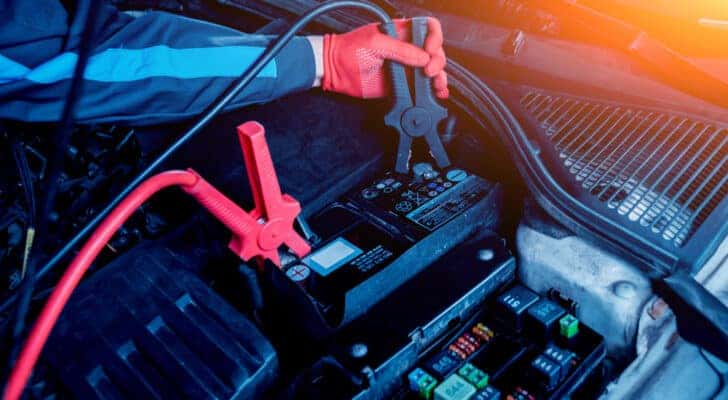 A mechanic is shown attaching plugs to a car battery.