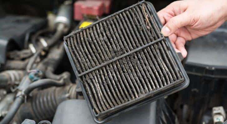 A mechanic is shown holding a dirty car air filter.