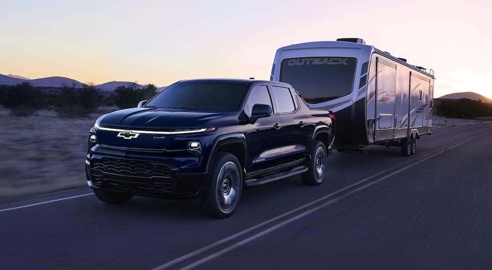 A black 2024 Chevy Silverado EV towing an RV on the highway.