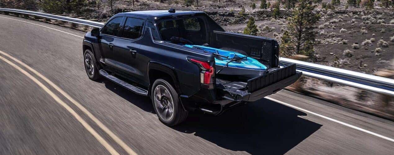 A black 2024 Chevy Silverado EV RST is driving on an open road.