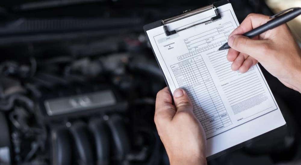 A technician is shown holding a clipboard near an engine bay.