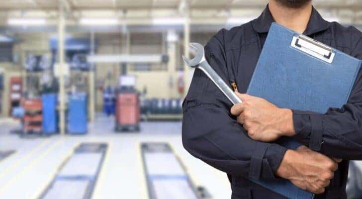 A technician is shown holding a clipboard and a wrench at a Toyota service center.