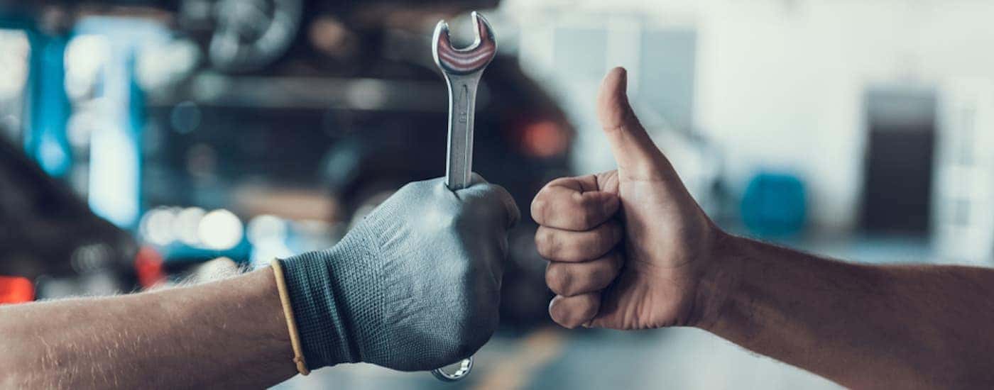 A hand throwing a thumbs up to another gloved hand holding a wrench.