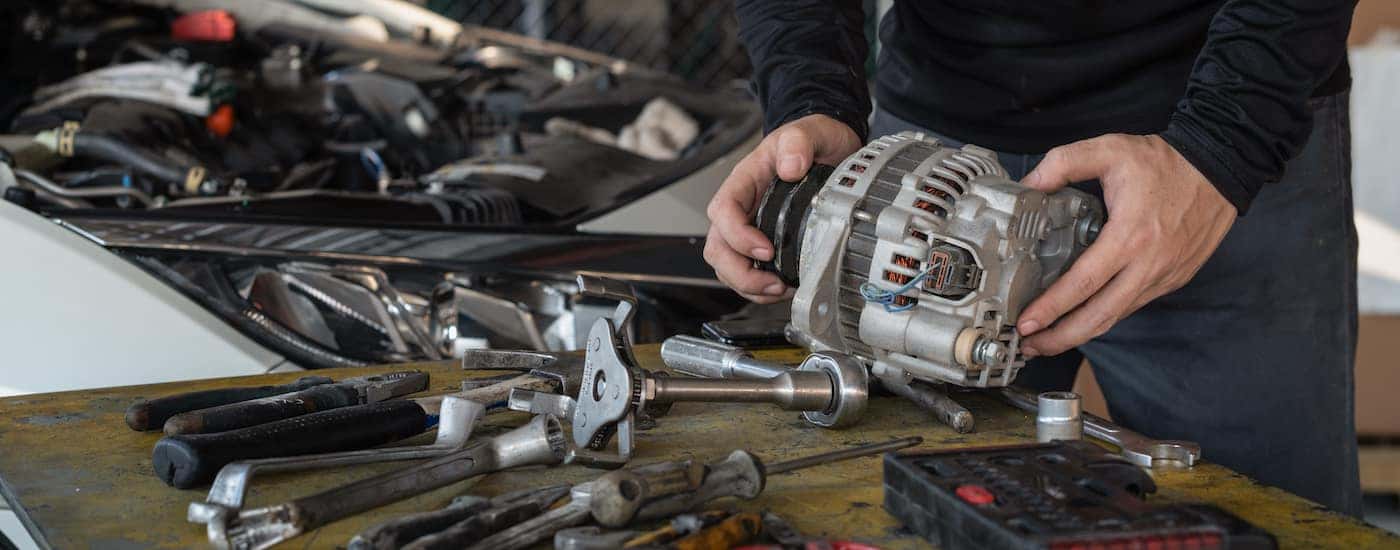 A mechanic holding an alternator on a table.