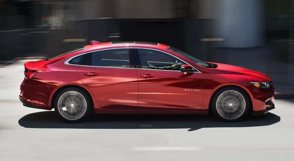 A red 2018 Chevy Malibu Hybrid is shown driving on a city street.