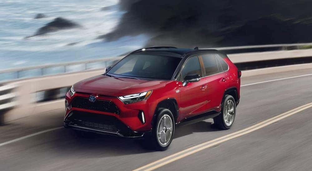 A red 2024 Toyota RAV4 Prime is shown driving near an ocean.