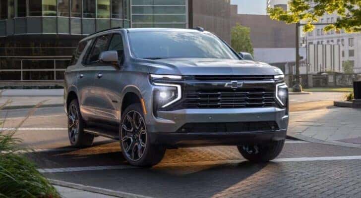 A silver 2025 Chevy Tahoe for sale is shown driving in a city.