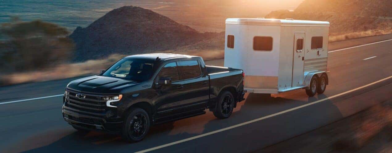 A 2025 Chevy Silverado 1500 High Country Black Edition is shown towing a trailer.