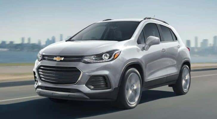 A silver 2021 Chevy Trax driving in front of a city skyline.