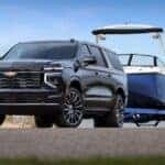 A blue 2025 Chevy Suburban High Country is shown towing a boat.