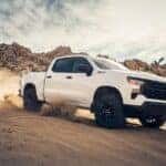 A white 2024 Chevy Silverado 1500 Custom Trail Boss off-roading through sand.