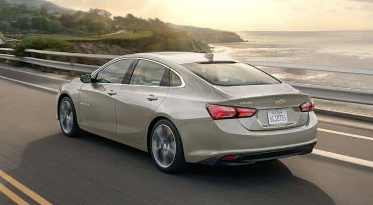 A tan 2023 Chevy Malibu is shown driving on a bridge.