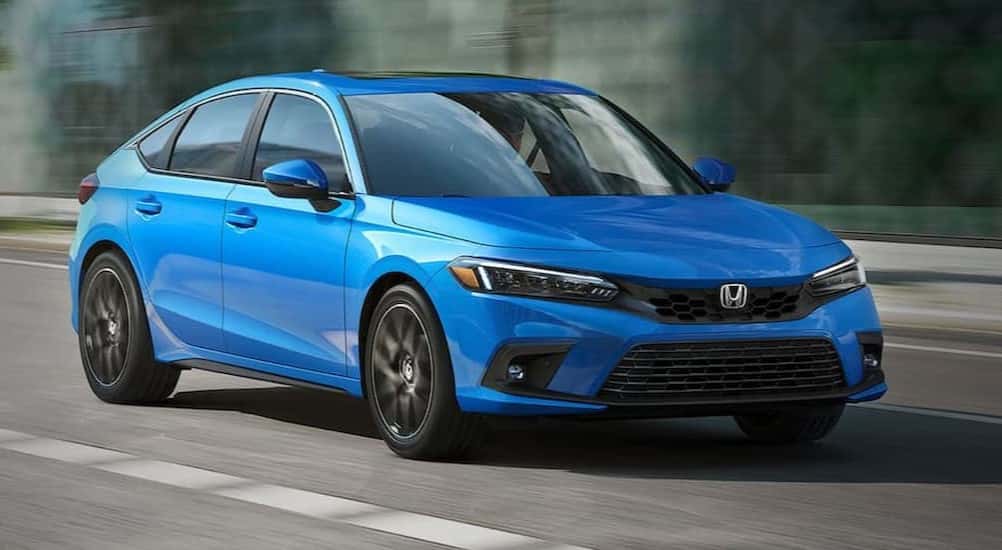 A blue 2022 Honda Civic Hatchback Sport Touring is shown driving on a highway.