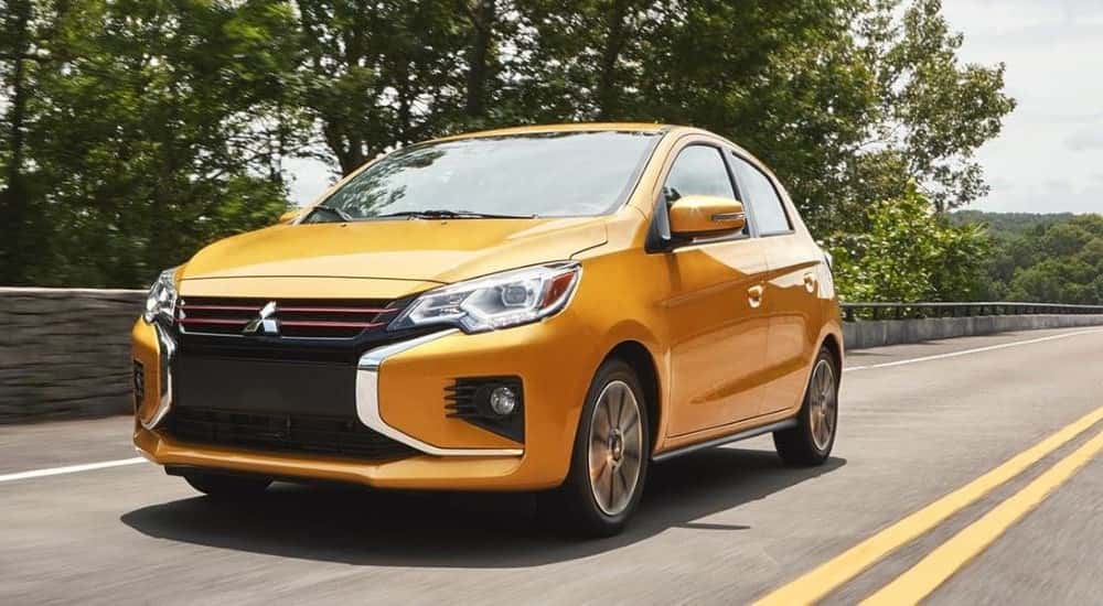 A yellow 2023 Mitsubishi Mirage is shown driving on a highway.