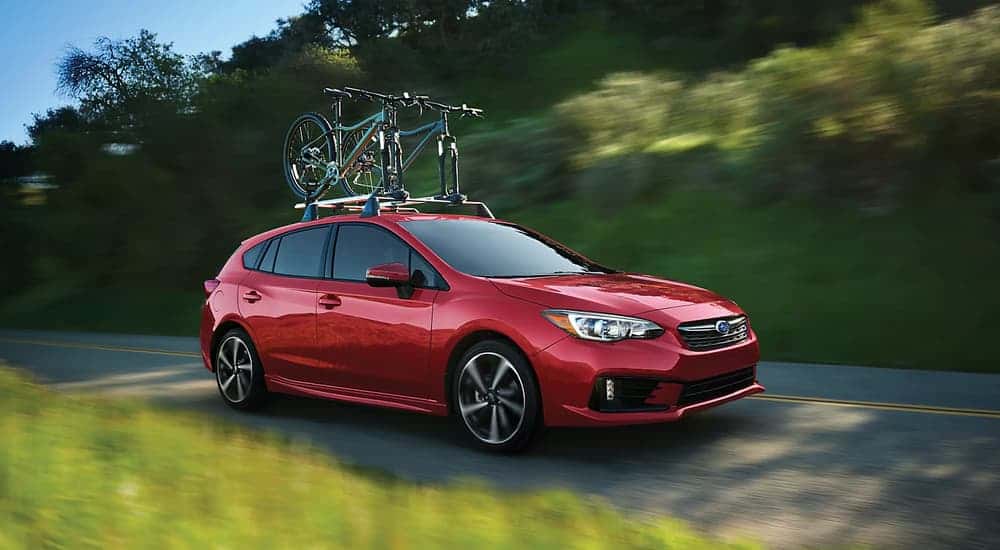 A red 2023 Subaru Impreza is shown driving with two bicycles on the roof.