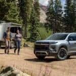 Two people walking towards a grey 2025 Chevy Traverse parked off-road.