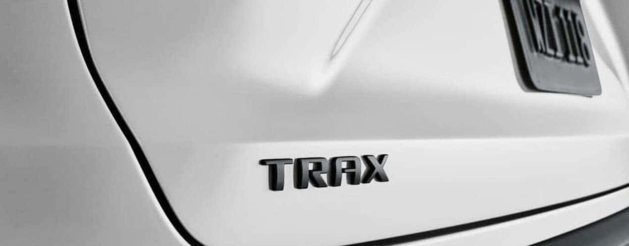 A close-up of the Trax badge is shown on the tailgate of a white 2025 Chevy Trax LT.