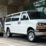 A white 2025 Chevy Express Passenger Van parked by a curb.