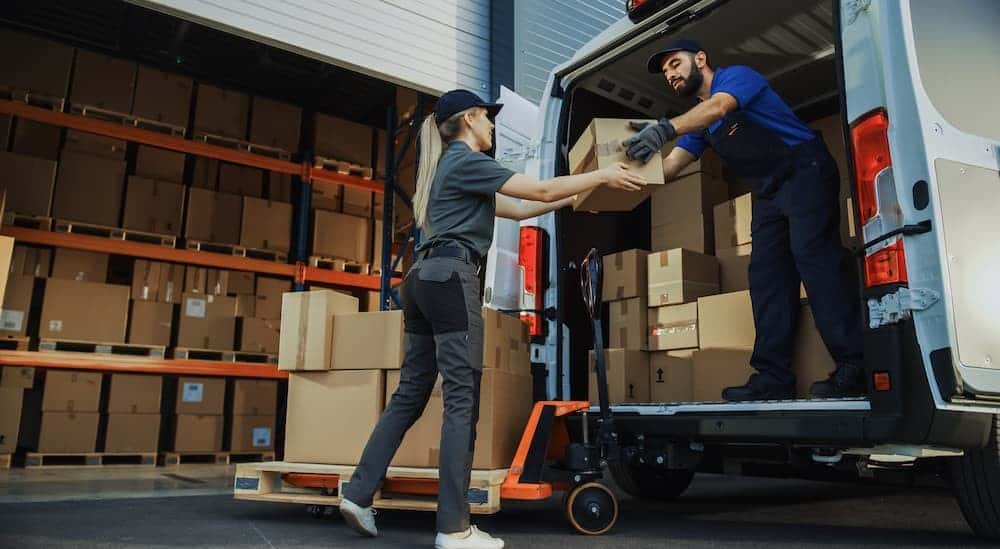 Two people are shown unloading boxes from the cargo area in a van.