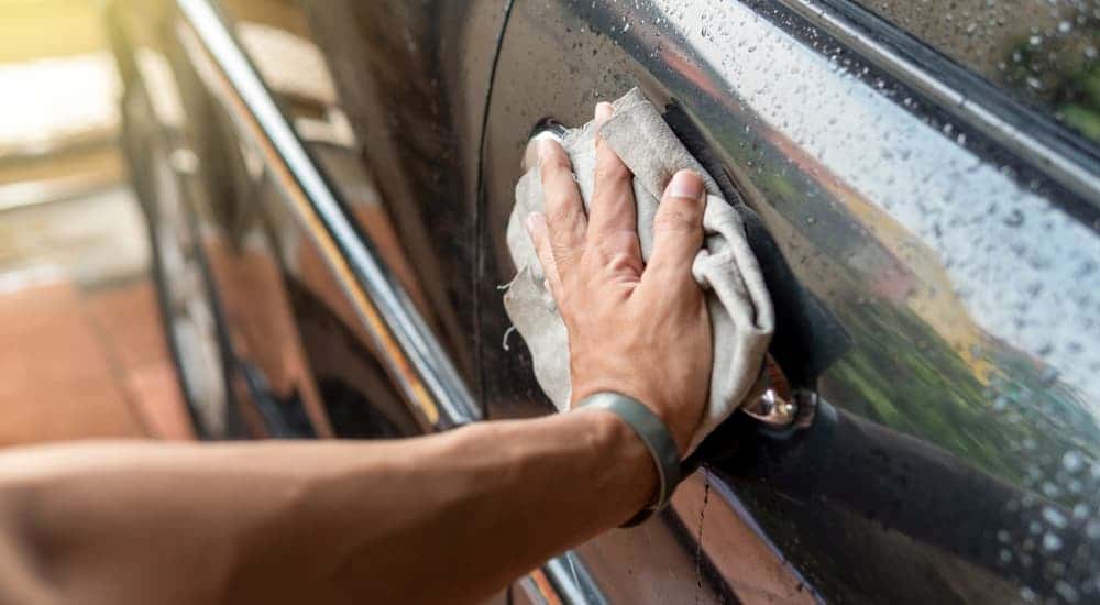 A hand wiping down a black car.
