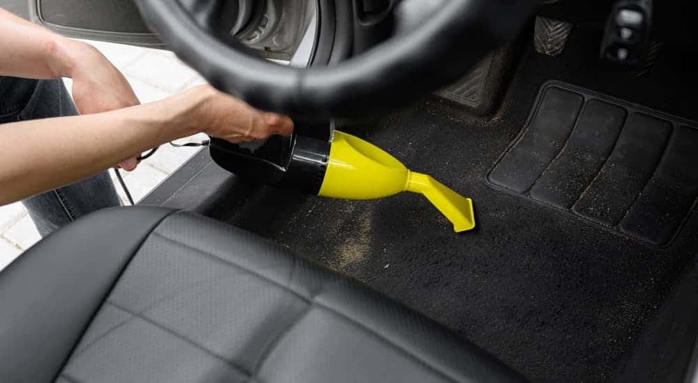 A person vacuuming the driver side floor mat in a car.