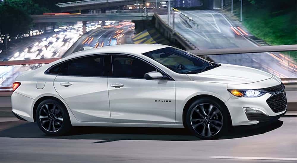 A white 2025 Chevy Malibu Midnight Edition driving on an overpass.