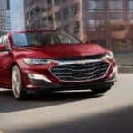 A red 2025 Chevy Malibu for sale in Cincinnati driving on a bridge.