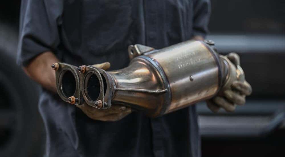A technician holding a catalytic converter at a GMC service center near Florence.