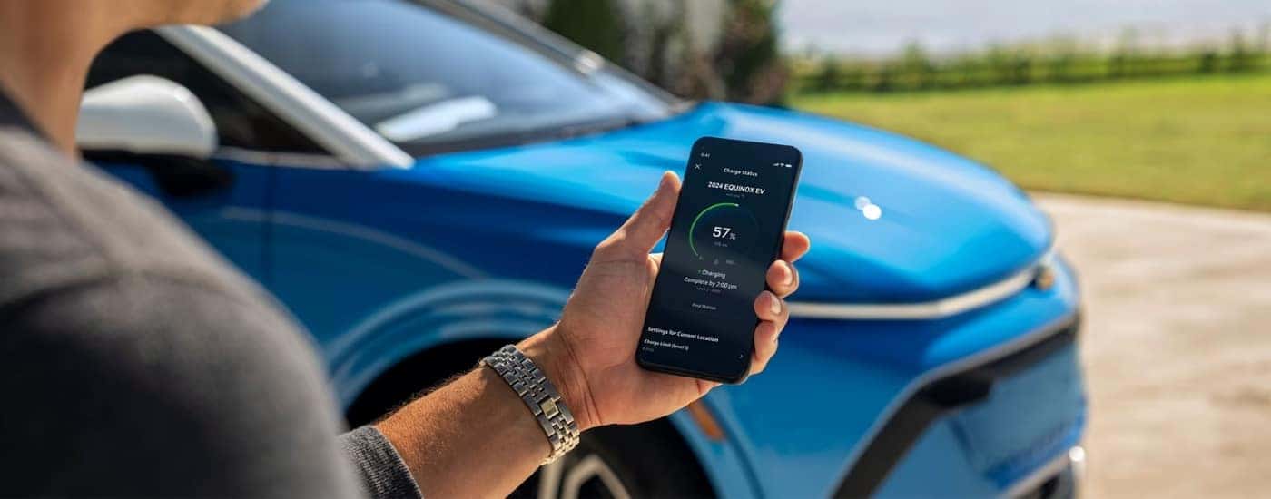 A person holding a smart phone near a blue 2025 Chevy Equinox EV.