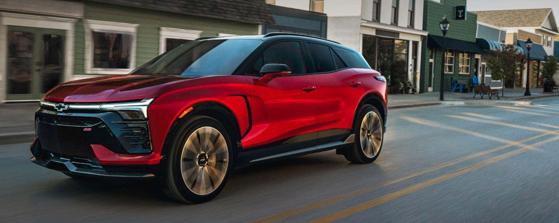A red 2025 Chevy Blazer EV RS driving past shops.