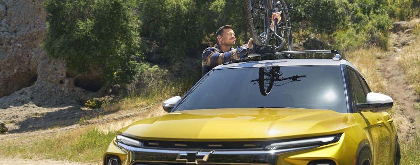 A man loading a bike on top of a yellow 2025 Chevy Trailblazer.