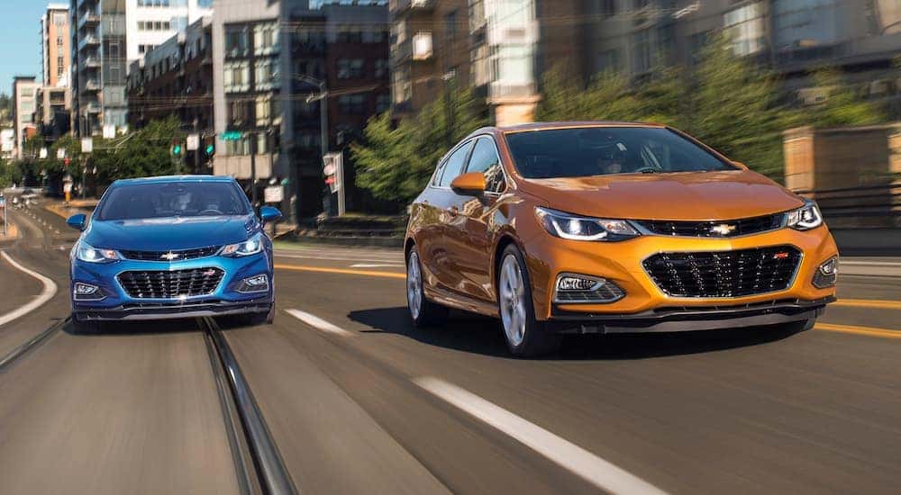 A blue and an orange 2018 Chevy Cruze driving on a city street.